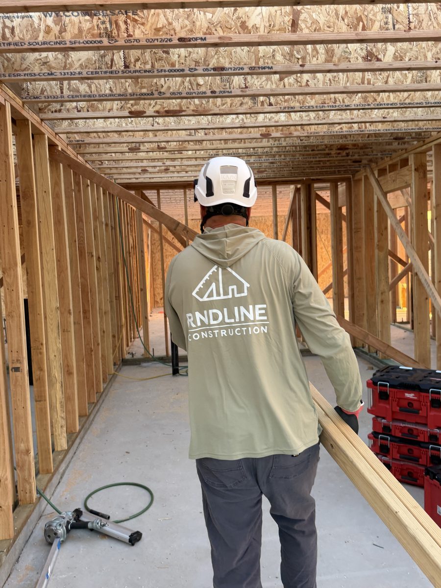 Carpenter in RNDLine workwear carrying framing lumber through a new addition