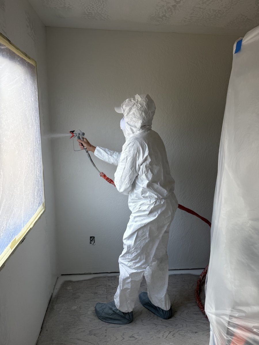 Painter spray-finishing a wall in protective coveralls