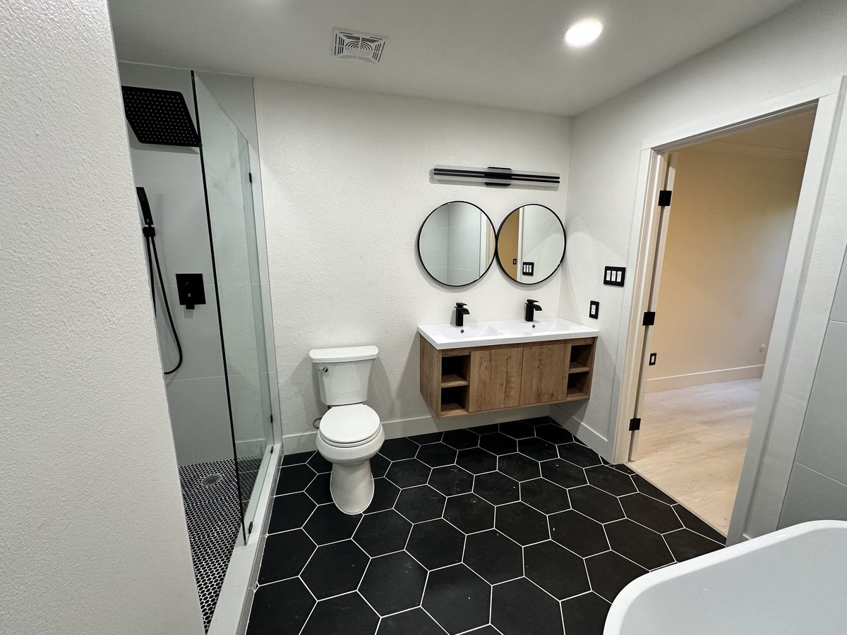 Bathroom remodel with a walk-in shower, floating wood vanity and black hex tile floor