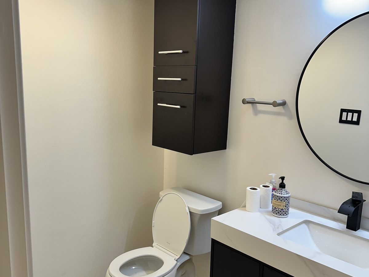 Compact guest bathroom with a floating dark vanity and round mirror